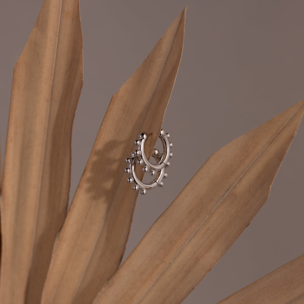 Beaded Hoops earrings, adorned with polished beads on silver hoops, are elegantly displayed on dried beige palm leaves against a muted background.