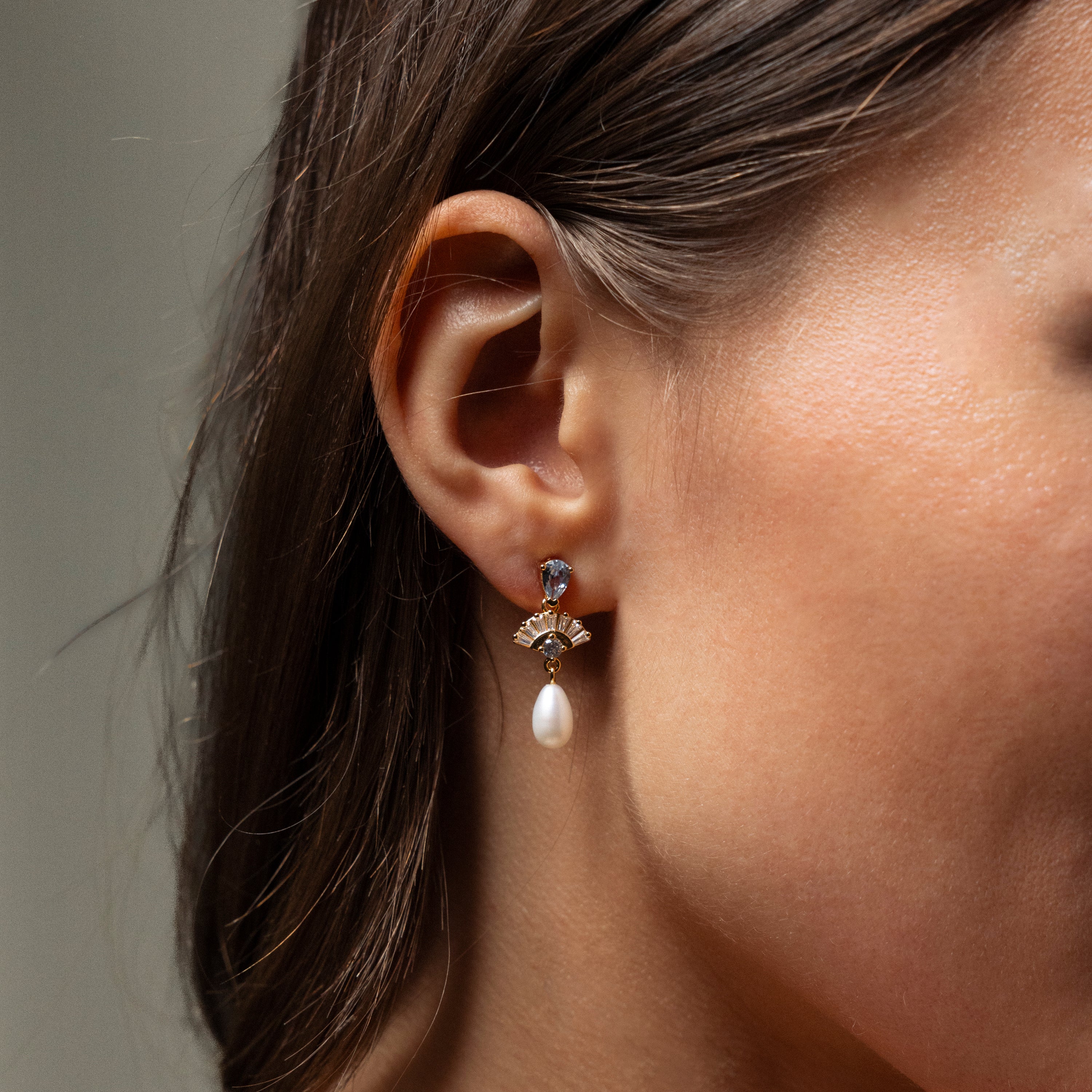 Close-up of a womans ear wearing Aquamarine Pearl Drop Earrings in 18K Gold, exuding vintage glamour with shimmering gemstones and a dangling pearl—an elegant choice for weddings.
