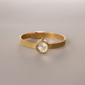 Gold round braided watch with a textured band displayed flat on a neutral surface.

