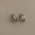 The Bold Multi Knot Studs in silver feature an intricate knot design, embodying modern elegance against a light beige background.