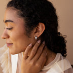 Woman with curly hair in a sheer cream blouse and silver floral earrings, showcasing the Pave Checkered Huggies in Silver as chunky hoops for a modern touch.
