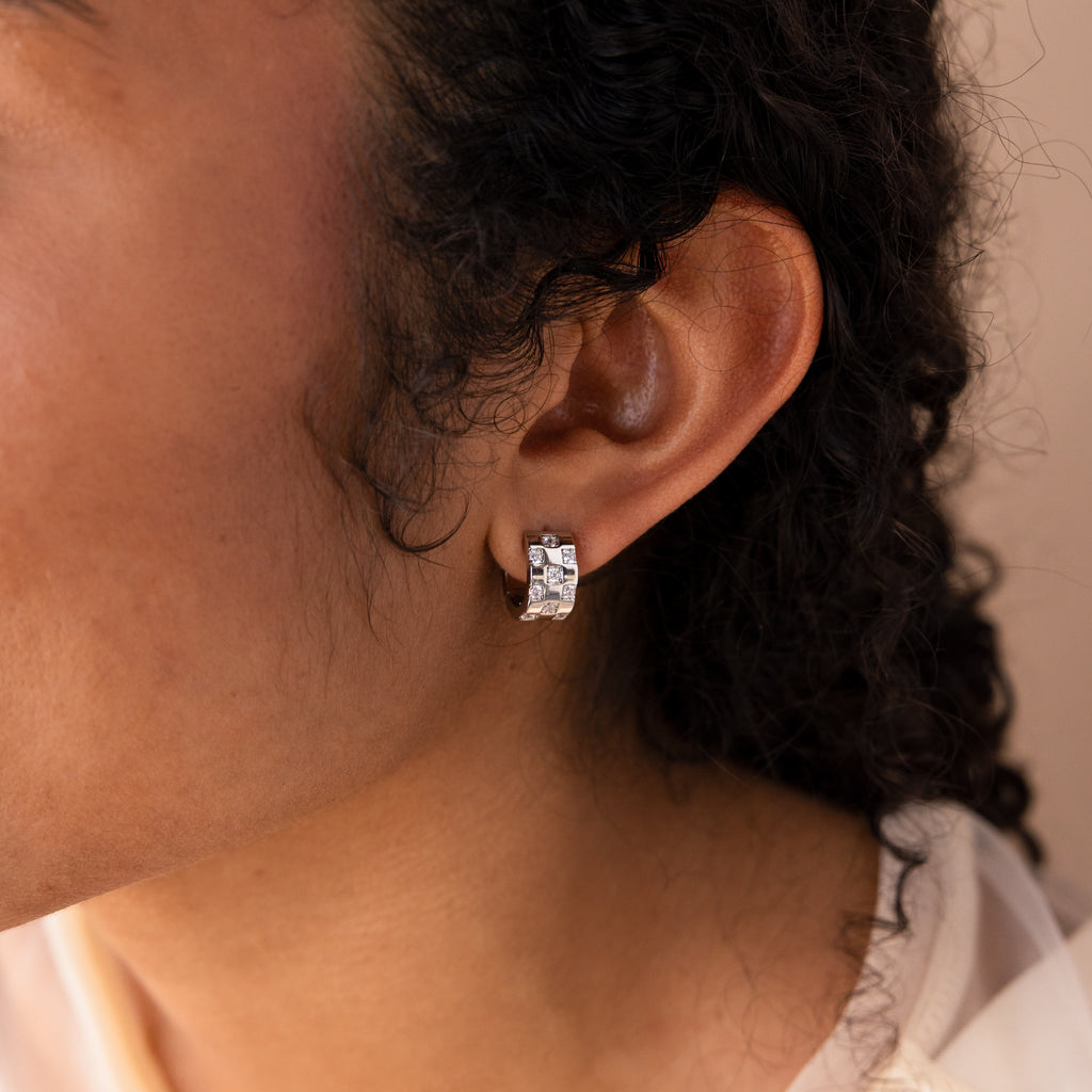Close-up of a person with curly hair wearing the Pave Checkered Huggies in Silver—chunky hoops with square-shaped stones for a bold statement look.