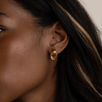 Close-up of a woman with dark hair and a blonde streak wearing Micro Triple Knot Earrings and layered gold hoops for an effortless quiet luxury look.