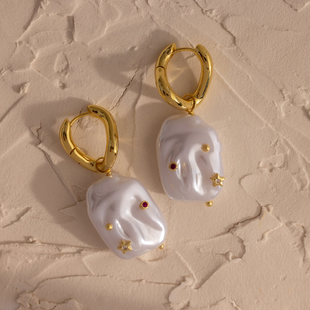 Celestial Baroque Pearl Charm Hoops in 18K Gold showcase irregular white pearls on gold hoops, accented with delicate gold, red, and star charms for a unique celestial-inspired look.