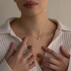 Woman wearing a cream ribbed shirt and the Dainty Duo Pearl Necklace, featuring two pearls, gently touching her chest.