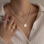 A person wearing pearl rings and a Dainty Duo Pearl Necklace, featuring pearls and a gold pendant engraved with the letter K.