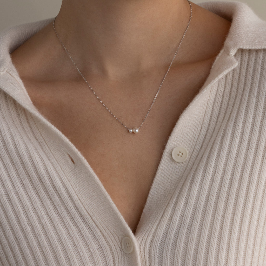 A person wearing a ribbed cream cardigan and the Dainty Duo Pearl Necklace in Silver.