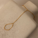 The Beaded Hand Chain Bracelet in 18K Gold, displayed on a beige textured surface, is a stunning statement piece that pairs beautifully with a delicate chain ring.