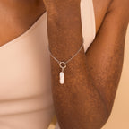A person wears the Long Baroque Pearl Charm in Sterling Silver, a versatile chain bracelet featuring a dangling pearl that effortlessly complements any style.