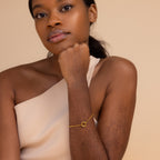 A woman in a one-shoulder top poses with her chin on her hand, highlighting the elegant Rolo Circle Charm Bracelet, featuring a detachable hinged circle for adding charms and personalizing your look.