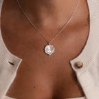 Close-up of a person wearing the Baby Hand & Footprint Necklace as a pendant, paired with a cream-colored cardigan fastened with one button.