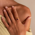 A hand adorned with the Birthstone Drop Chain Ring, featuring a purple gemstone, rests gently on a bare shoulder.