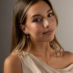Woman with long hair wearing a beige dress and the Opal Star Necklace & Earrings Set in 18K Gold, smiling softly.