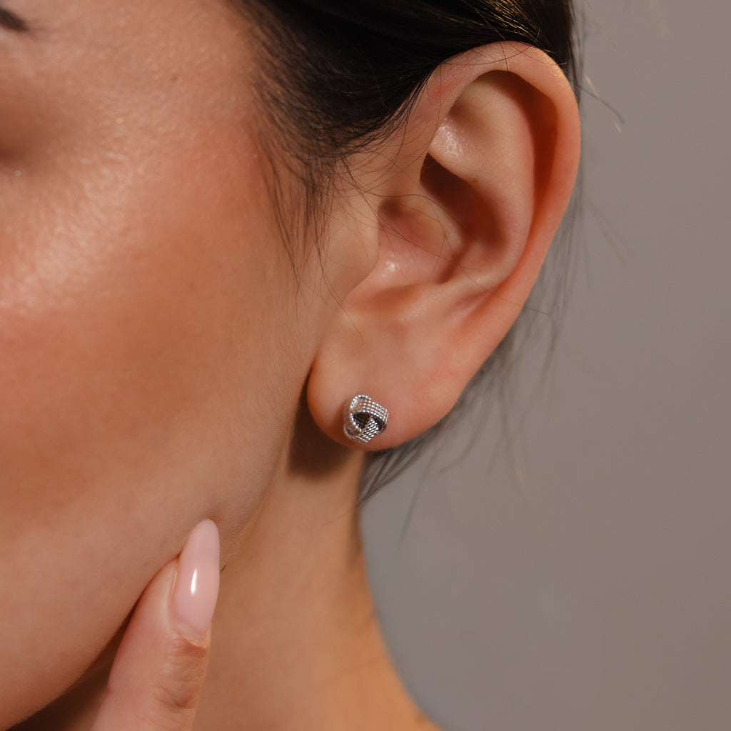 Close-up of a woman's ear wearing Rope Knot Studs in Silver; her finger touches her chin, showcasing the elegant, round silver earrings—perfect minimalist jewelry for any occasion.