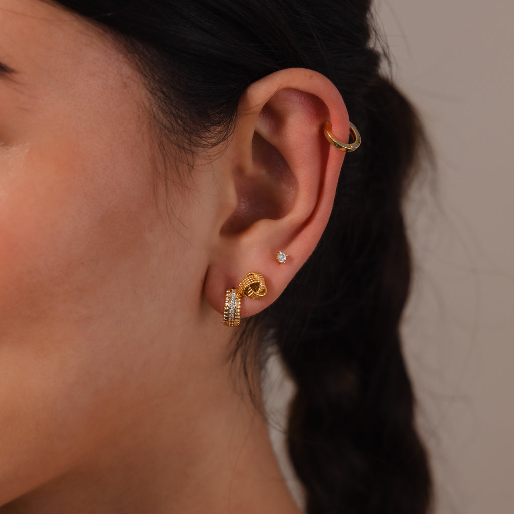 A close-up of an ear with Rope Knot Studs, three gold earrings, and a small diamond stud, paired with stylish braids—perfect inspiration for your next earring stack.