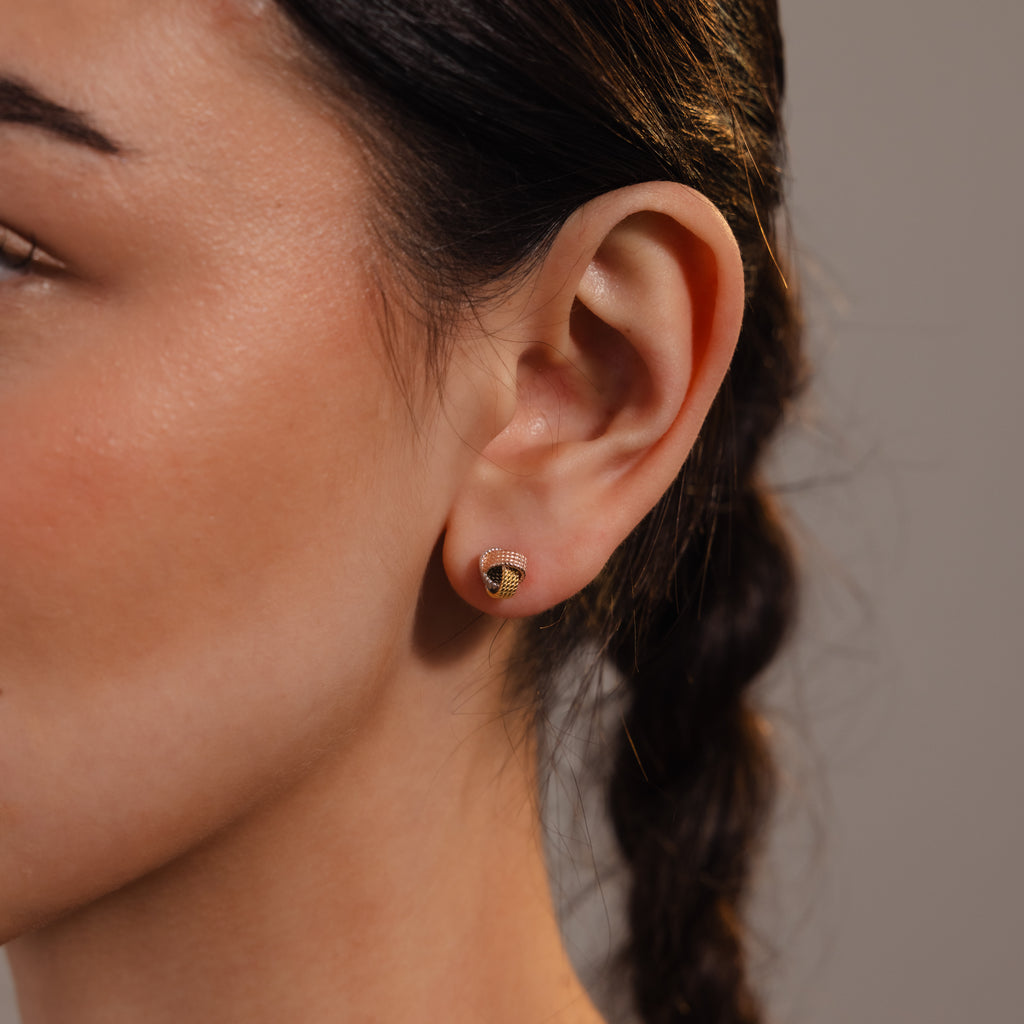 Close-up of a woman's ear wearing Rope Knot Studs in Mixed Metal, featuring a minimalist design. A braid is visible in her dark hair, emphasizing the simple yet elegant accessory.