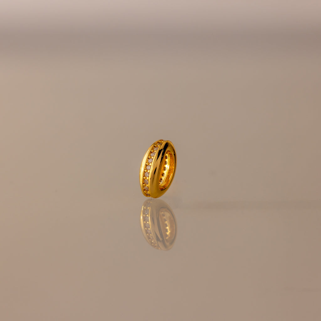 The Pave Dome Charm in 18K Gold gleams on a reflective surface, capturing every sparkle against a soft gradient background—a dazzling piece to elevate any charm stack.