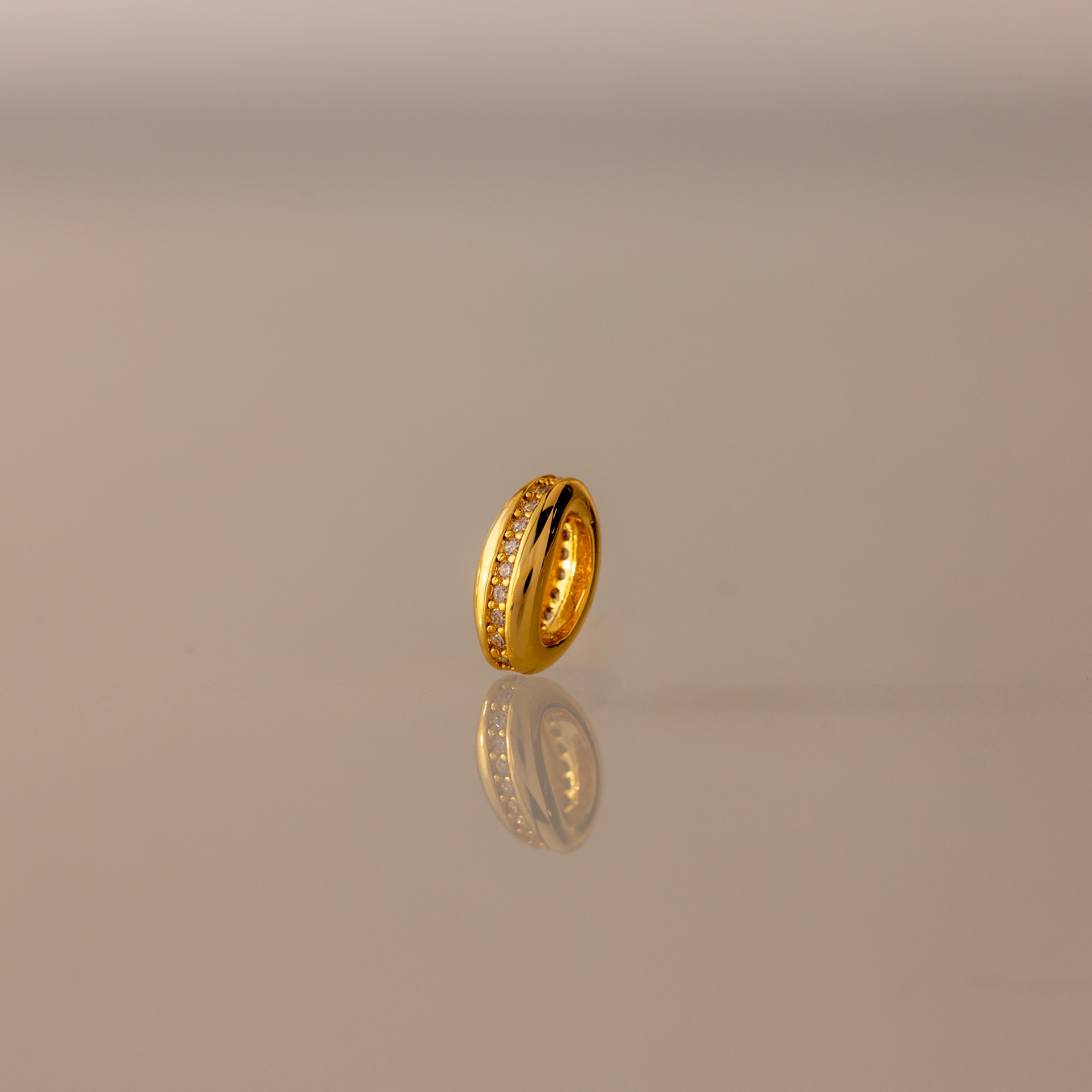 The Pave Dome Charm in 18K Gold gleams on a reflective surface, capturing every sparkle against a soft gradient background—a dazzling piece to elevate any charm stack.
