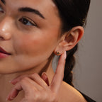 A woman with braided hair gently points to her Rope Knot Studs in Mixed Metal, her soft smile drawing attention to the elegant earrings.