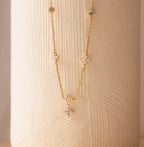 The Ivy Diamond Station Necklace features diamond-shaped and round gemstone accents, evoking a floral design, displayed on a textured beige surface.