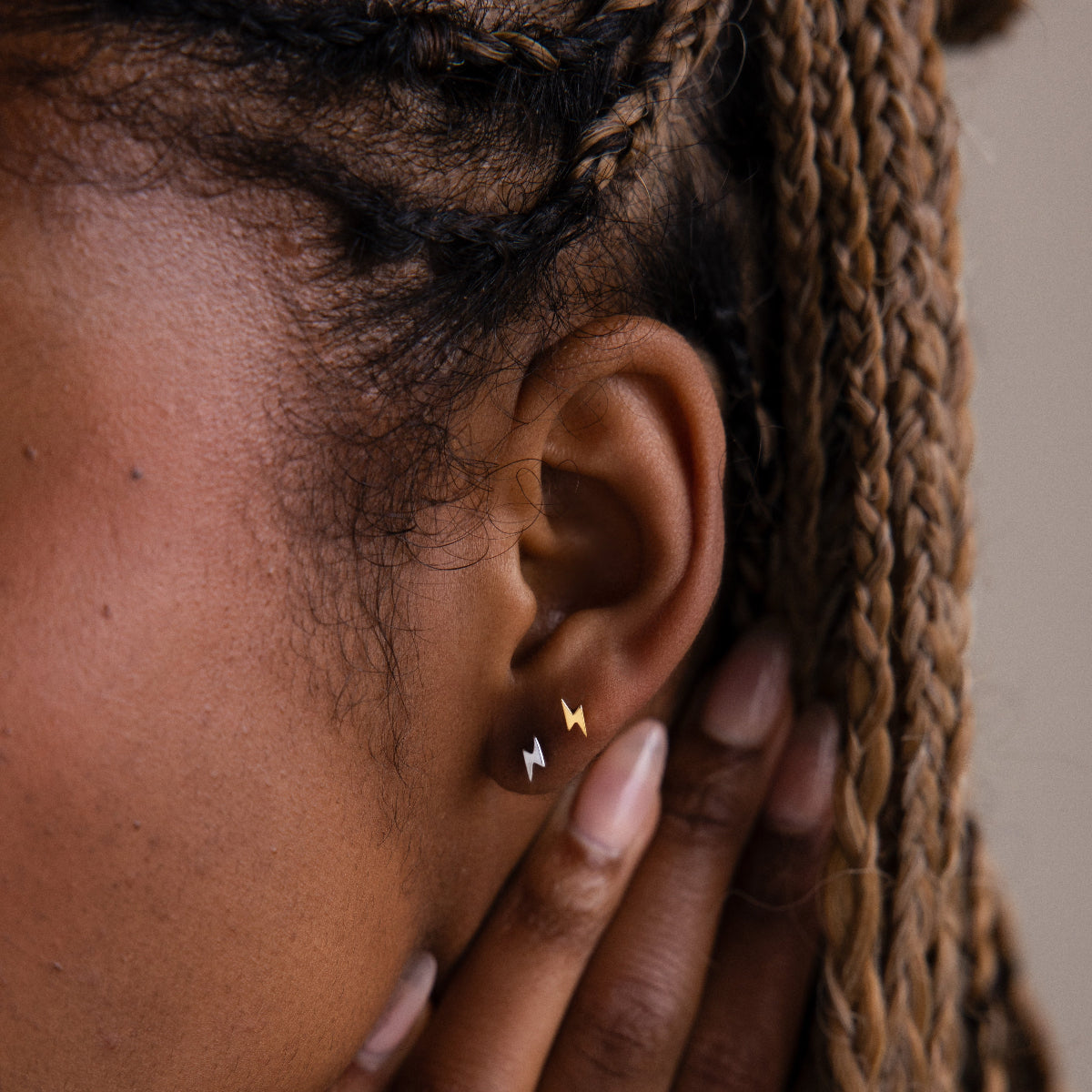 Close-up of a model with gold and silver lightning bold stud earrings and braided hair.
