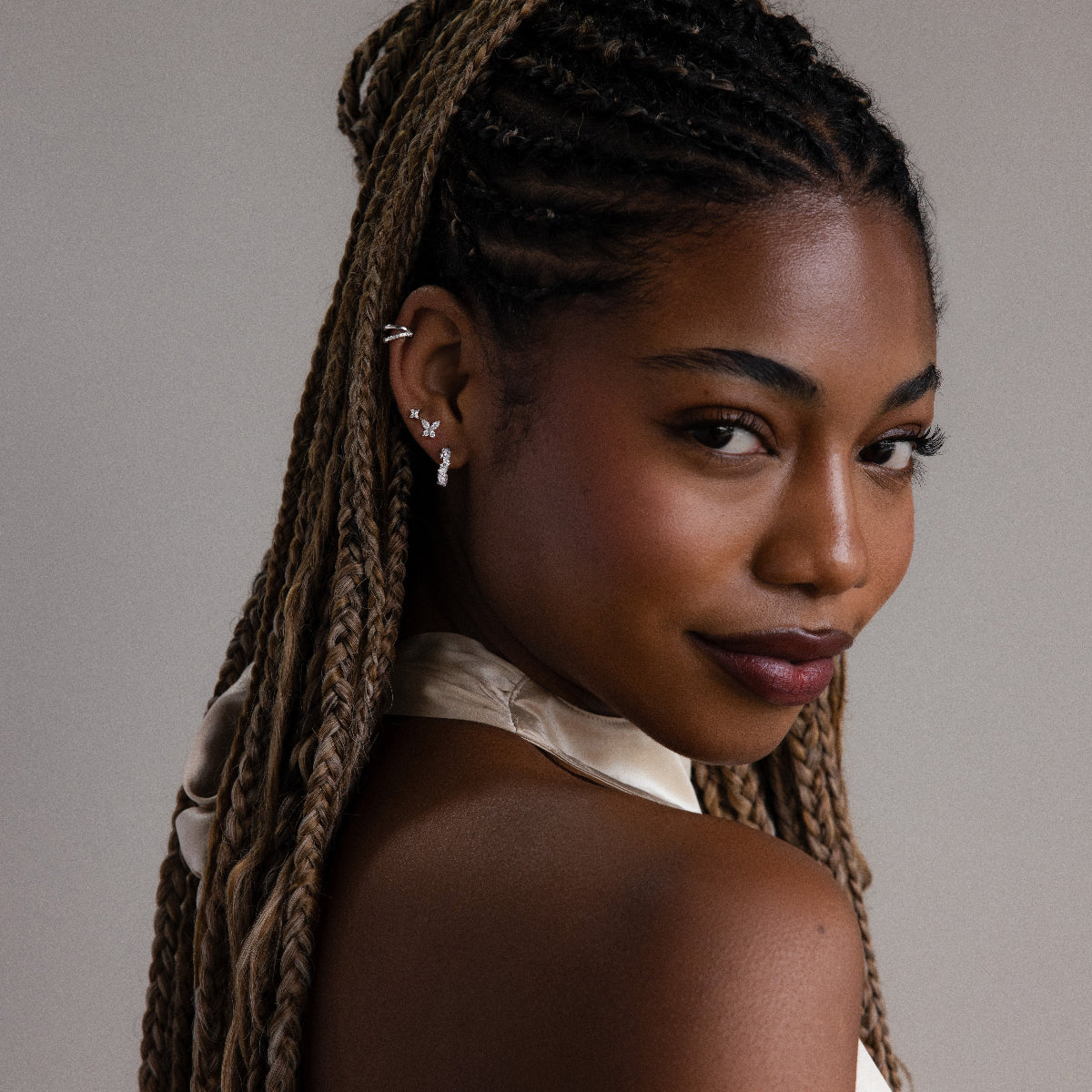 Woman with braided hair wearing silver diamond earrings against a neutral background