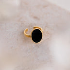The Midnight Hour Onyx Ring features a large oval black stone and an adjustable band, elegantly displayed on a light beige marble surface.