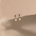 Heart Pearl Drop Earrings in Silver with heart-shaped studs and dangling pearls, elegantly displayed on a textured beige background.