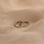 Two slim silver Classic Diamond Sprinkle Huggies with small clear stones set along the front, resting on draped beige fabric.