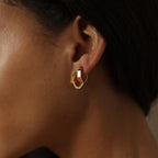 Close-up of a model wearing gold hoop earrings with a dark background