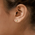 Close-up of a model wearing a gold earring with a turquoise gemstone.