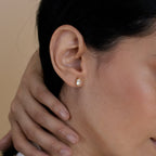 Close-up of a model with a gold diamond earring against a neutral background