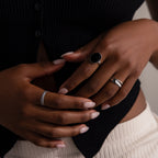 Close-up of manicured hands wearing a black ribbed top and cream pants, styled with the Midnight Hour Onyx Ring, a vintage-glam accessory featuring an adjustable band.