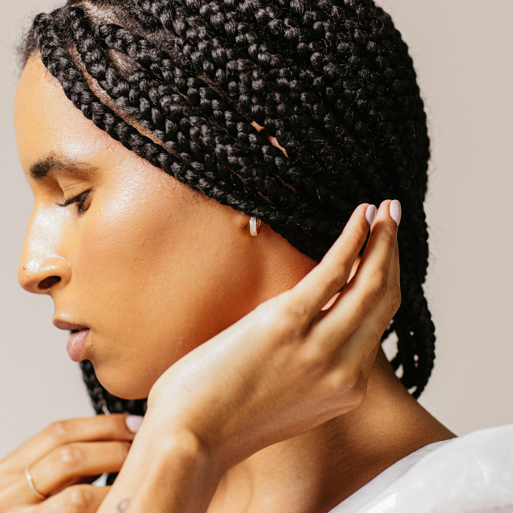 Woman with braided hair wearing a diamond hoop earring against a neutral background