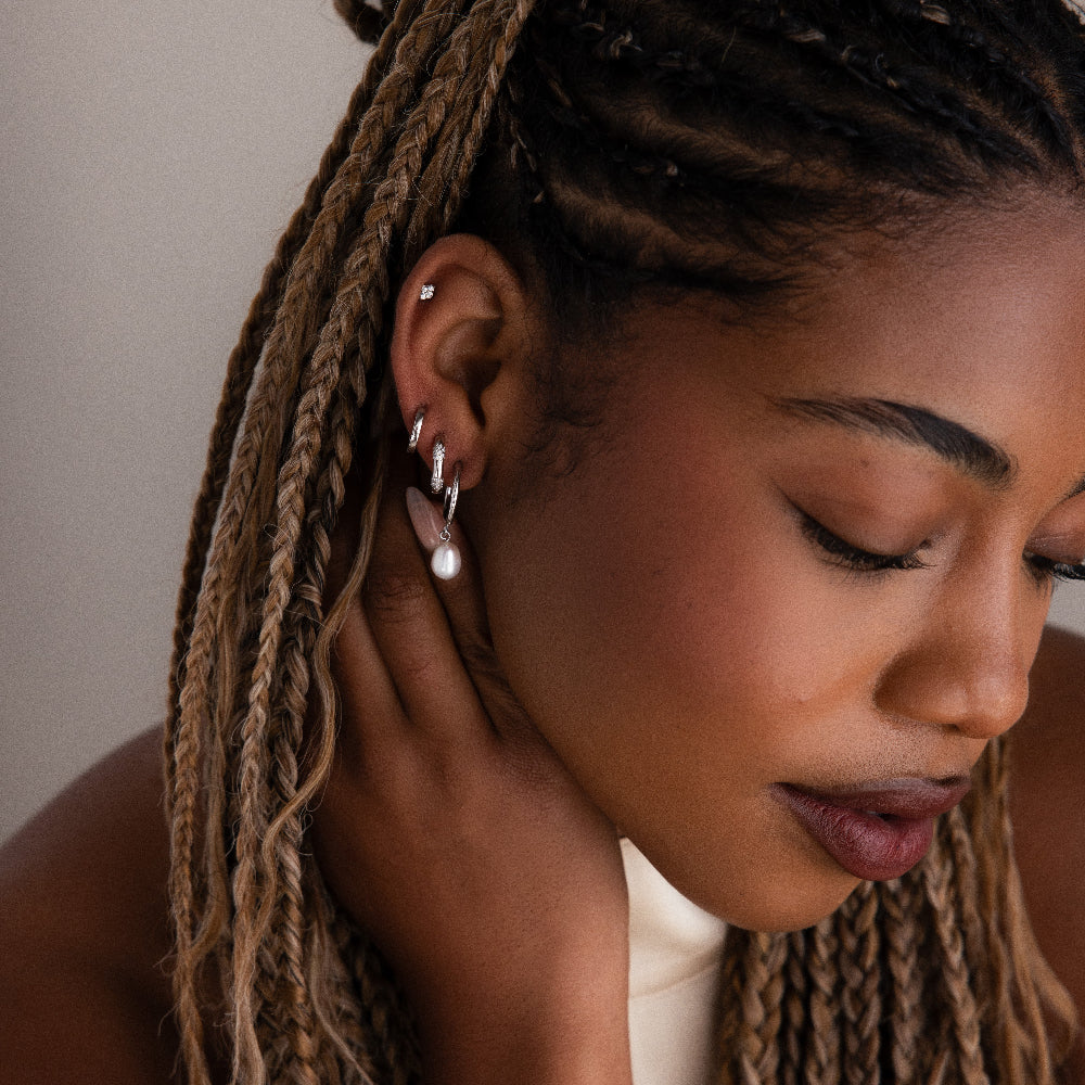 Close-up of a woman with braided hair wearing various silver earrings against a neutral background
