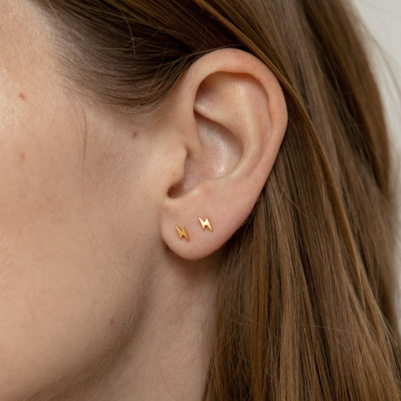 Side profile of a model wearing dainty gold lightning bolt stud earrings, showcasing a simple and elegant everyday earring style.