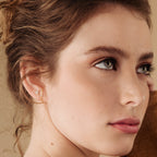 Close-up of a woman wearing gold diamond stud earrings with a neutral background