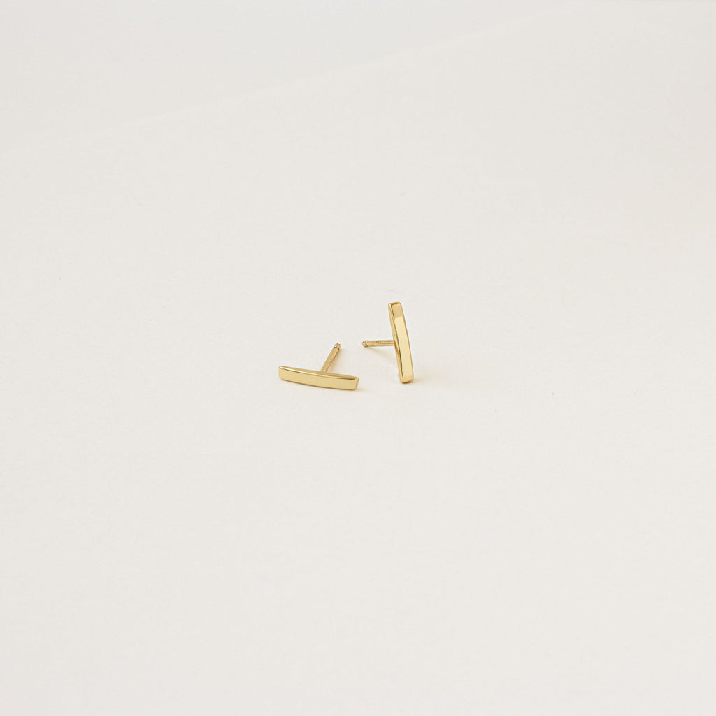 Gold bar earrings on a light beige background