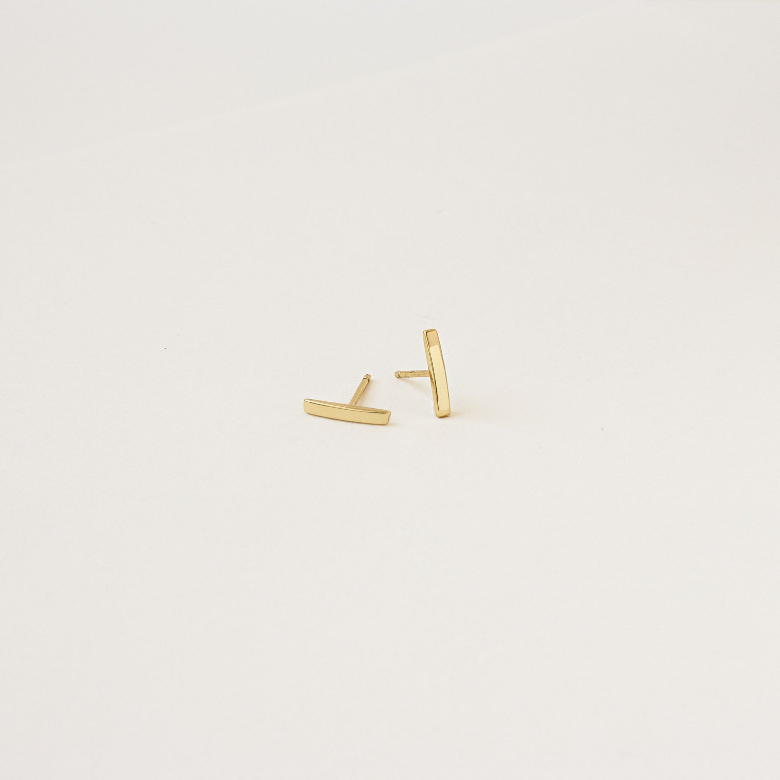 Gold bar earrings on a light beige background