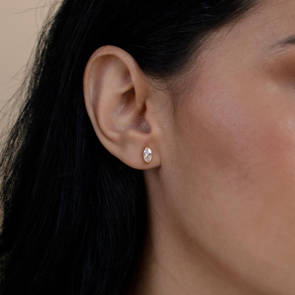 Close-up of a model wearing a diamond earring with dark hair and a beige background
