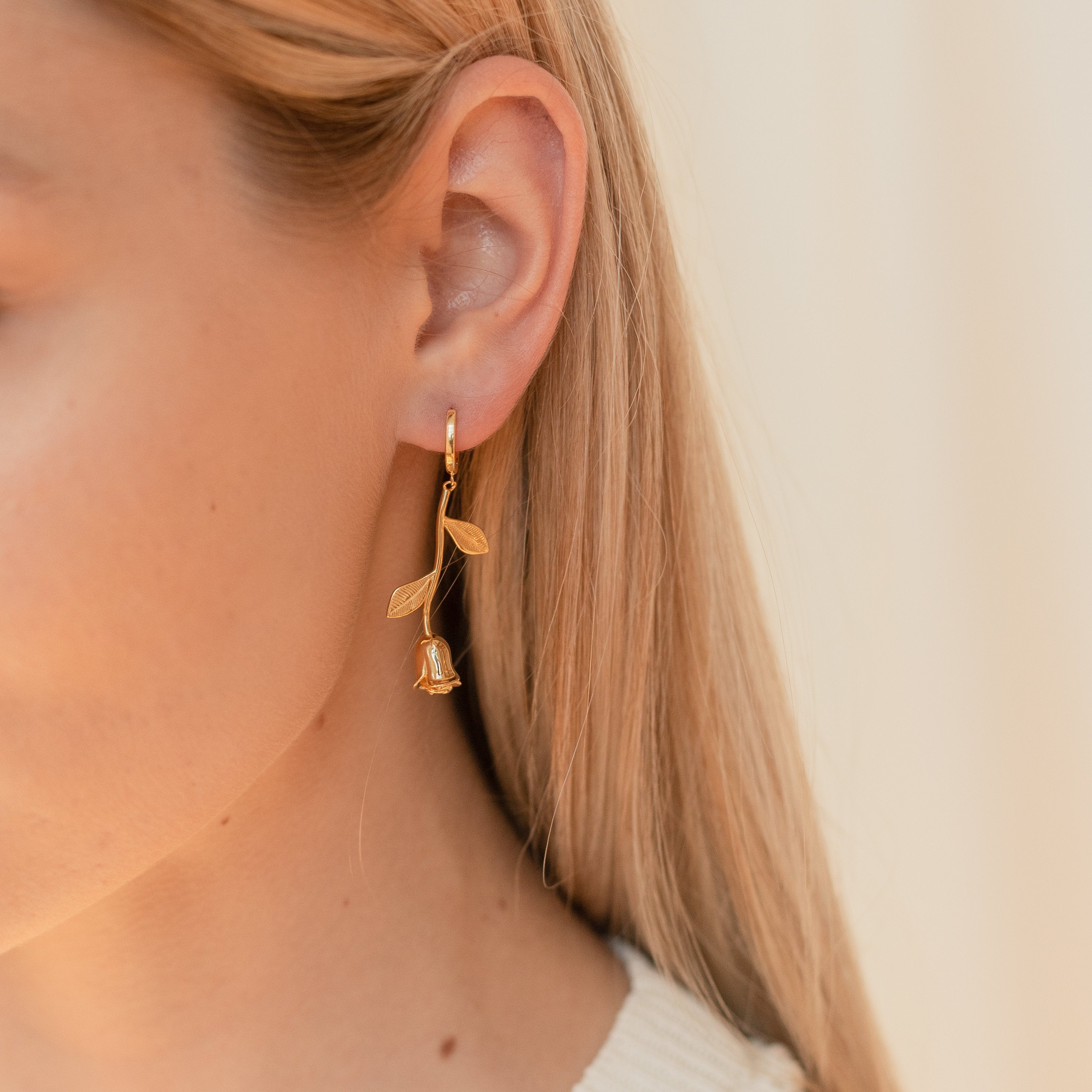 Close-up of a person wearing a gold floral earring against a neutral background