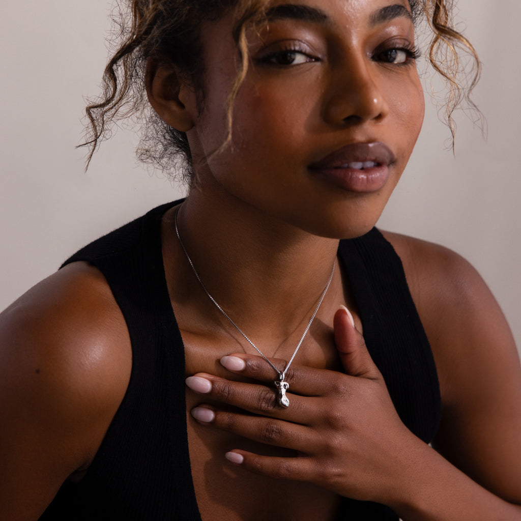 A woman in a black top touches her chest, showcasing the Kinn Body Necklace with a small silver body shaped pendant.