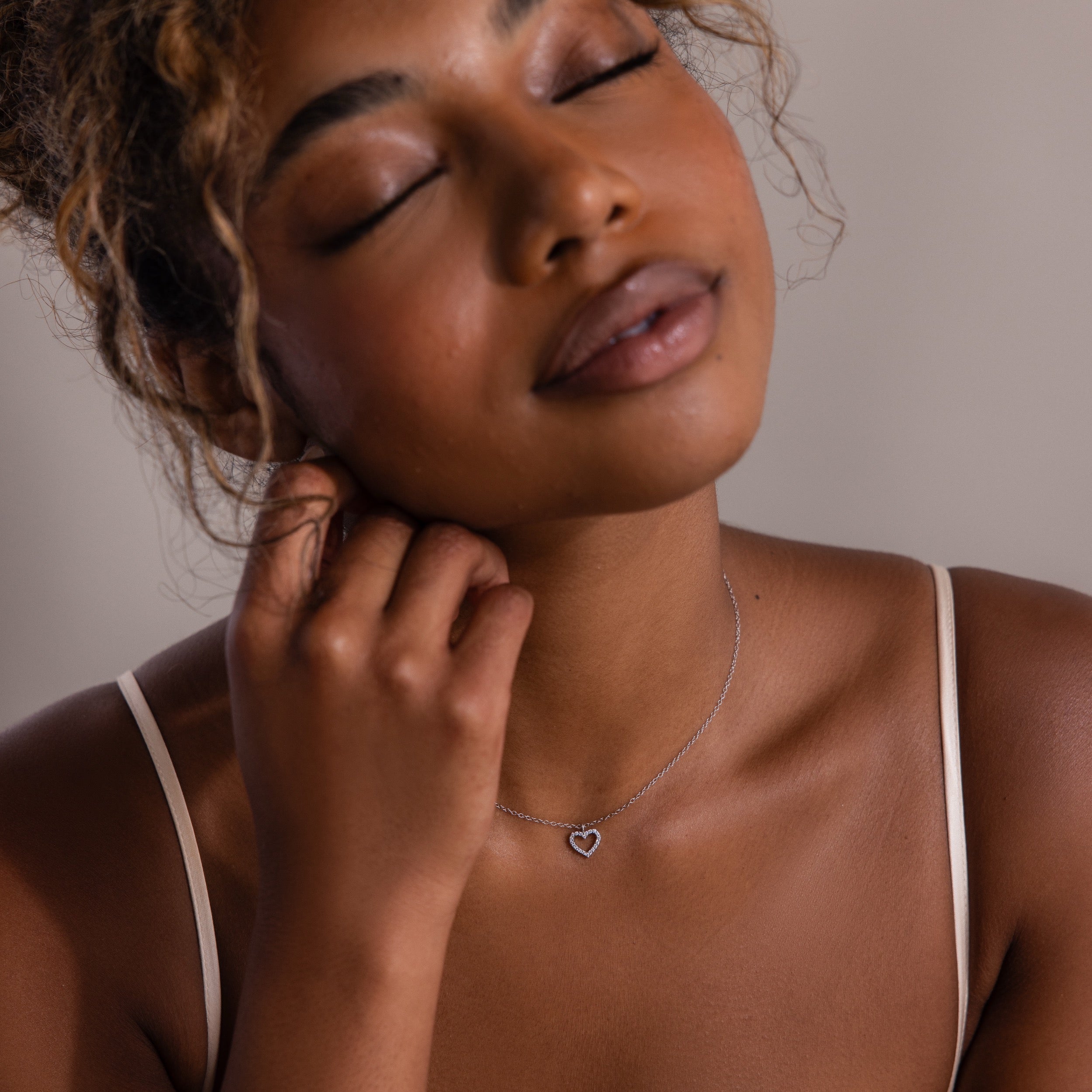 Woman with curly hair and closed eyes touches her neck, wearing the Forever Pave Heart Necklace—an elegant choice for bridal jewelry.