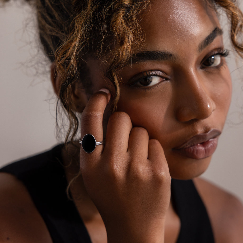 Woman with curly hair wears the Midnight Hour Onyx Ring, gazing at the camera while gently touching her face.