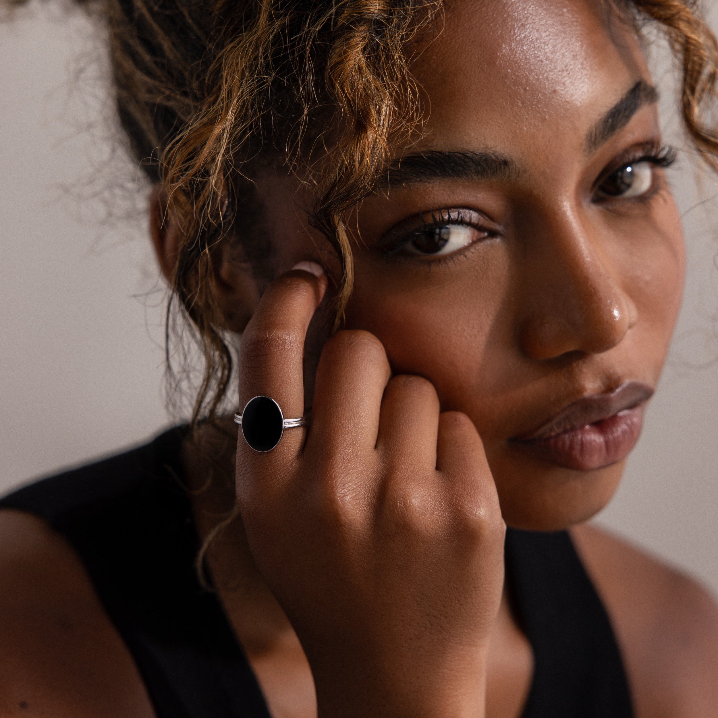 Woman with curly hair wears the Midnight Hour Onyx Ring, gazing at the camera while gently touching her face.