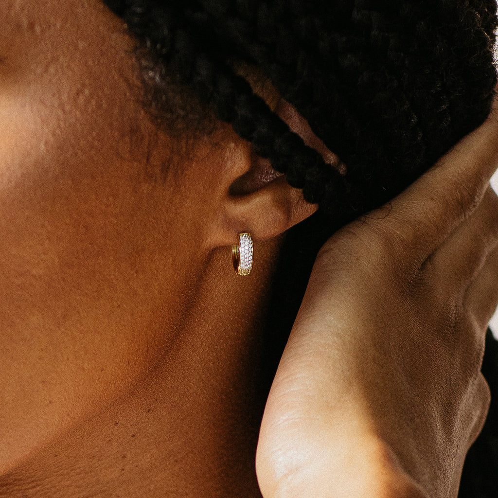 Close-up of an ear wearing a gold hoop earring with a blurred background