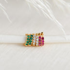 Five gold rings with green, white, and pink stones are displayed on white textured fabric—ideal to pair with subtle earrings or the Elise Diamond Huggies for an elegant look.