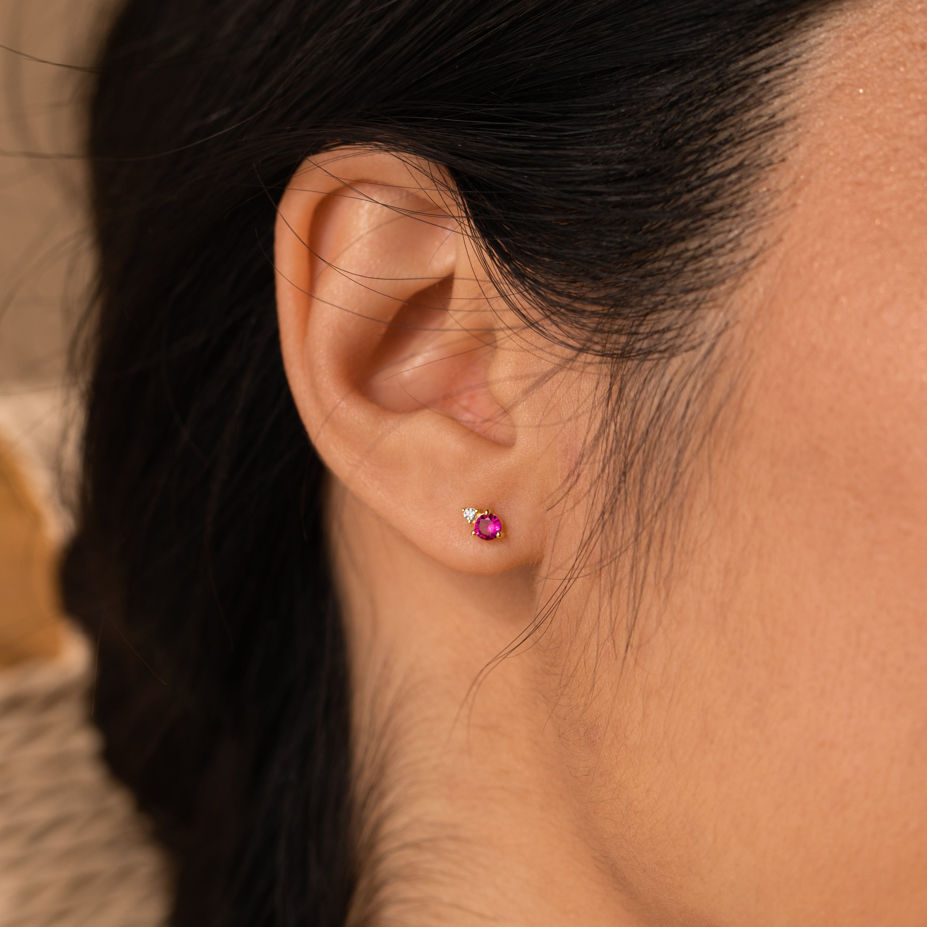 A close-up of an ear wearing the Raindrop Ruby Studs—a dainty pink ruby stud with a tiny diamond accent, perfect for fans of diamond earrings and birthstone studs.
