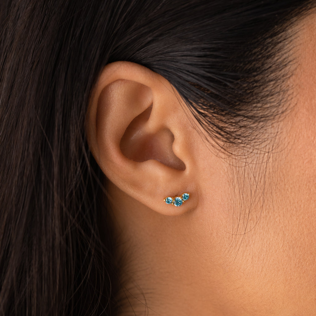 Close-up of a womans ear wearing Bella Birthstone Studs—a small, blue birthstone earring thats an elegant and personalized jewelry gift for mothers and daughters.