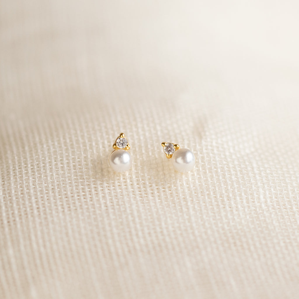 Raindrop Pearl Studs: gold and pearl earrings with small crystals, shown on a textured cream fabric background.